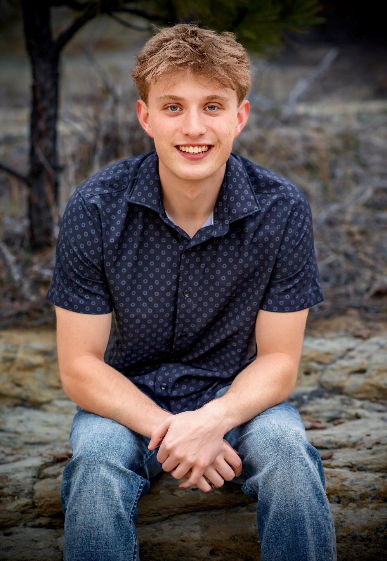Young man smiling outdoors, casual attire, natural background.