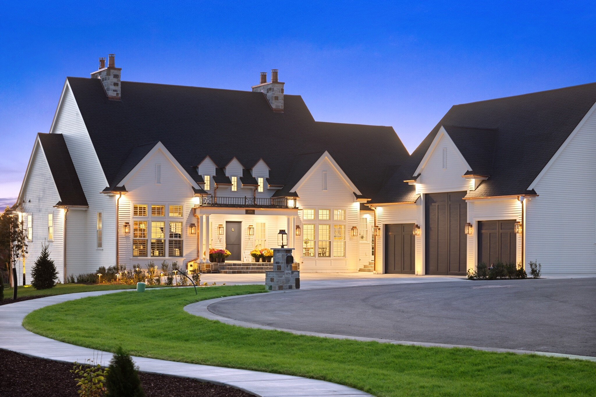 Elegant white suburban home with a spacious driveway and manicured lawn at dusk.