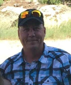 Construction worker wearing a plaid shirt and sunglasses outdoors at a building site.